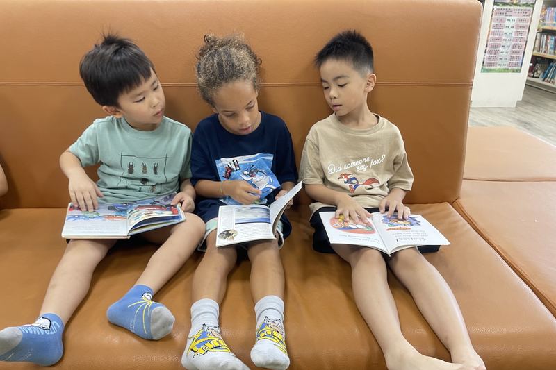 Three children reading together on a library sofa
